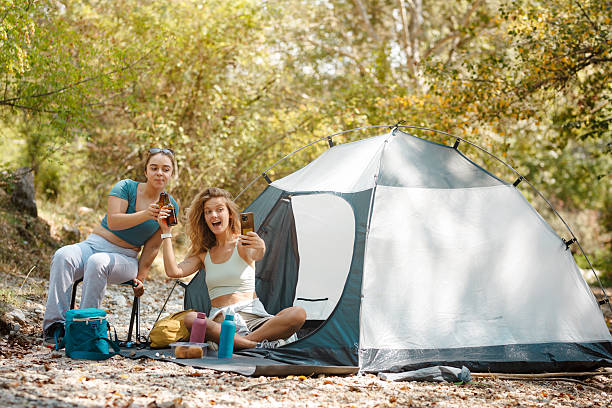 istock Friends enjoying a cheerful moment while camping in a forest during the day, capturing memories with their phones and relaxing outdoors 2247277074