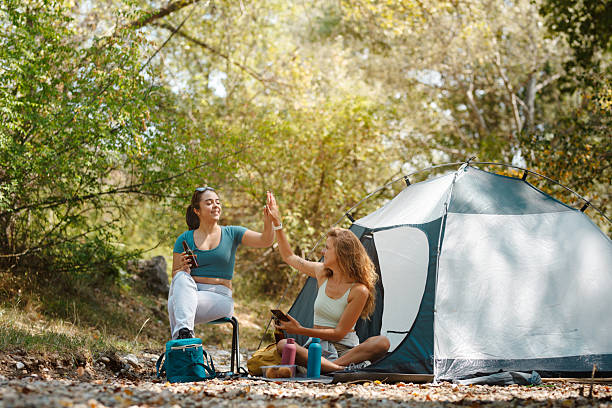 Two friends enjoying a fun moment while camping in a natural setting during a sunny day surrounded by trees