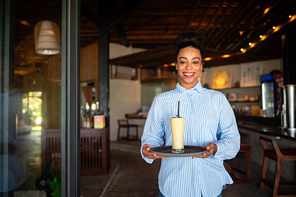 Close up of young smiling african american waitress serving fruit juice, smoothie while working in a cafe.. Happiness lifestyle concept.