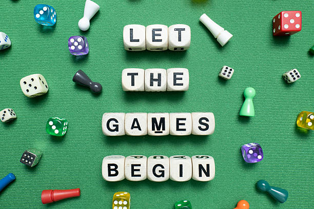 Wooden dice show the phrase 'Let The Games Begin' with a selection of colourful dice and game tokens lying around it on a vibrant green baize fabric