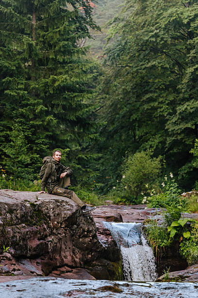istock Man Hiker Sitting on Rock by Flowing Water 2247280983