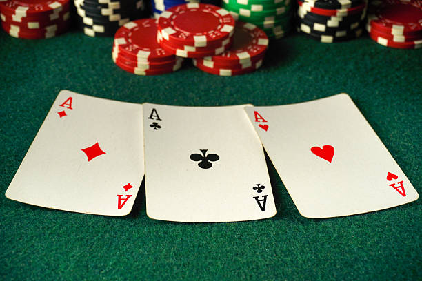 istock A poker table is set with three aces displayed prominently. Surrounding the cards are numerous colorful chips, indicating an active game. Players are engaged and focused on their hands 2247281580