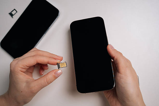 istock Woman holding sim card and new smartphone on white table, preparing for inserting sim card and activating mobile service for seamless connectivity and communication. 2247281820