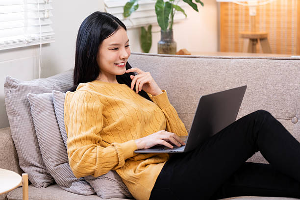istock Content and thoughtful young Asian woman working or browsing on her laptop while relaxing on the sofa at home in soft afternoon light 2247282833
