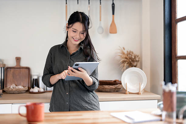 istock A smiling Asian woman happily using a digital tablet while standing in her contemporary kitchen. 2247284036