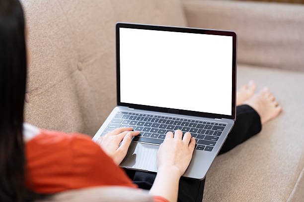 istock Close-up of a young woman's hands typing on a laptop with a blank white screen, working remotely from a sofa at home. 2247284332