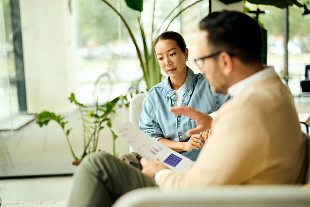 istock Asian Woman and Man Discussing Documents in a Bright Modern Office Lobby 2247285020