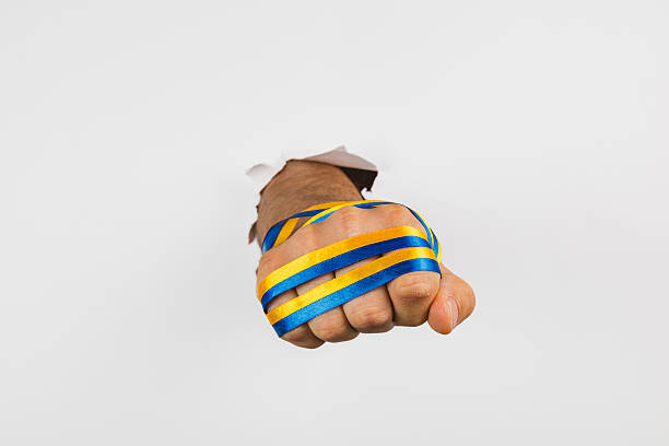 istock Fist breaking through wall with blue and yellow stripes for support 2247286068