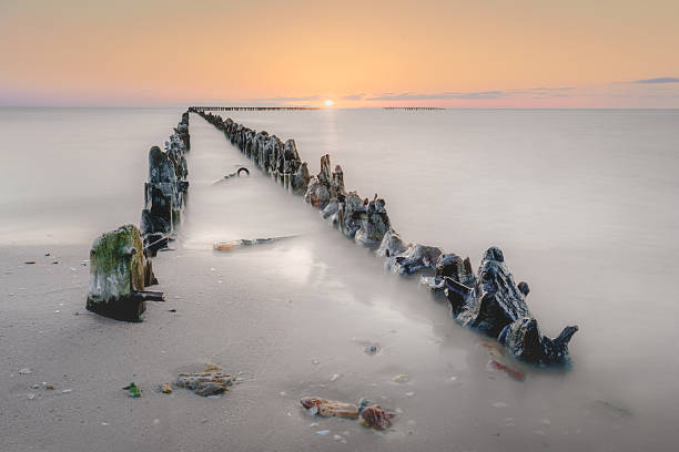 istock groynes lead through ethereal waters to a warm, glowing horizon. 2247286168