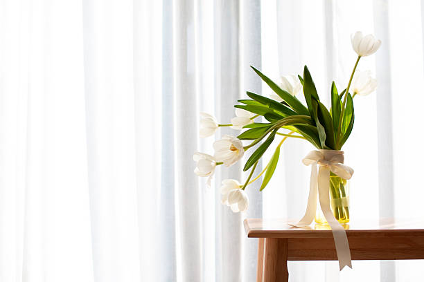 Bouquet of pink tulips in a transparent glass vase on a white table.