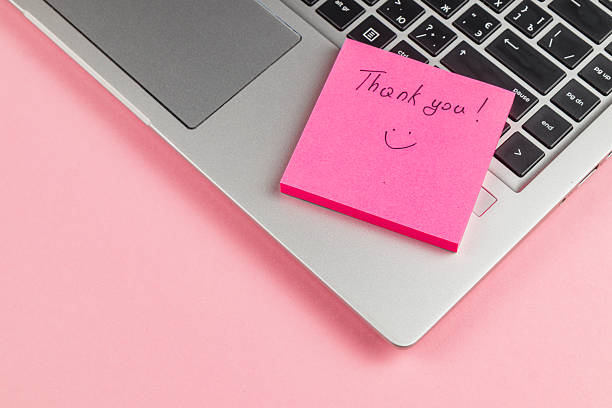 istock Thank you note on pink sticky pad next to laptop on a pink background 2247288709