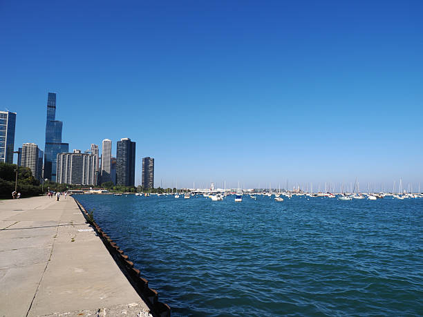 Calm blue waters of Lake Michigan extend under a partly cloudy sky at Chicago waterfront featuring a distant white sailing ship and a lighthouse during daylight hours.