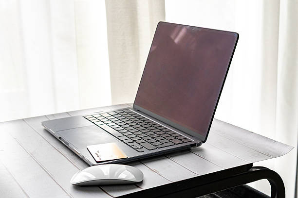 istock Modern laptop and wireless mouse on a wooden table near white curtains. 2247290390