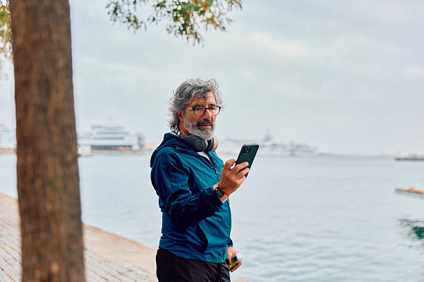 istock Senior man using smartphone with headphones outdoors 2247290568