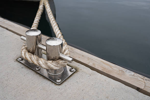 Boat cleat with rope on concrete dock, reflecting tranquil water surface, highlighting marine equipment and nautical elements in a peaceful setting
