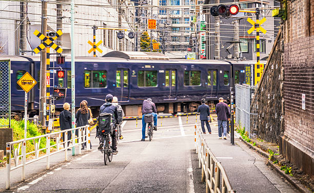 Tokyo, Japan - Pedestrians and cyclists waiting at a railroad crossing as a train passes.