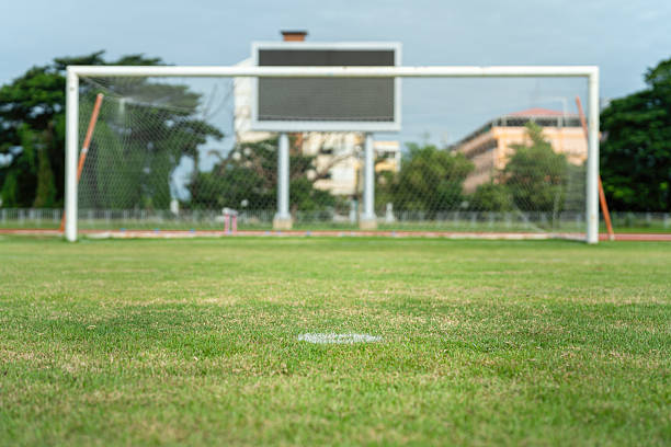 Football field with green grass ground, selective focus at penalty kick point as foreground and goal as blurred background.