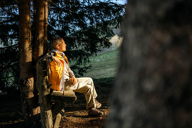 Female hiker takes a quiet break during her hike, basking in the warm sunlight that illuminates her face. Surrounded by natural scenery, she enjoys a peaceful and reflective moment outdoors