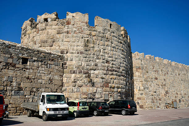 Kos, Greece - September 16, 2025:  Various vehicles are parked along the castle wall with battlements along the harbor of kos town