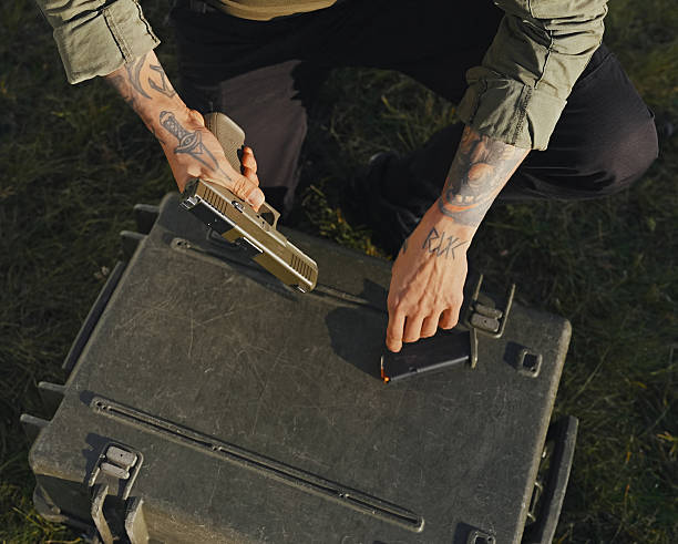 Trained soldier with hand tattoos performing the disassembly and the cleaning process of a pistol gun firearm in field conditions. Professional technician removing parts to clean and perform maintenance