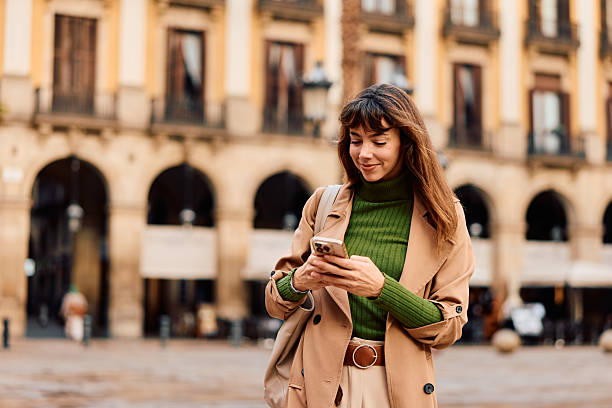 istock Young woman smiling, texting on phone in city square 2247298703