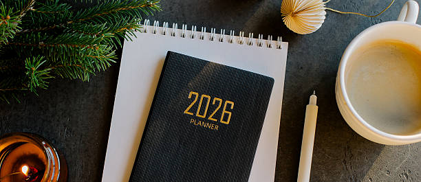Stylish Desk Setup With 2026 Planner, Notebook, Pencil, Glasses, Fir tree Branch and Coffee on Wooden Surface. Banner Image for design, web site
