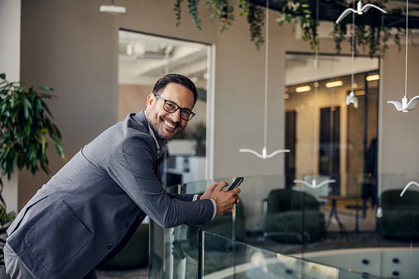 istock Mature adult businessman smiling and using mobile phone in modern office 2247299364