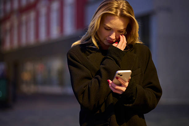 istock Blond young woman standing in street at night text messaging 2247300595