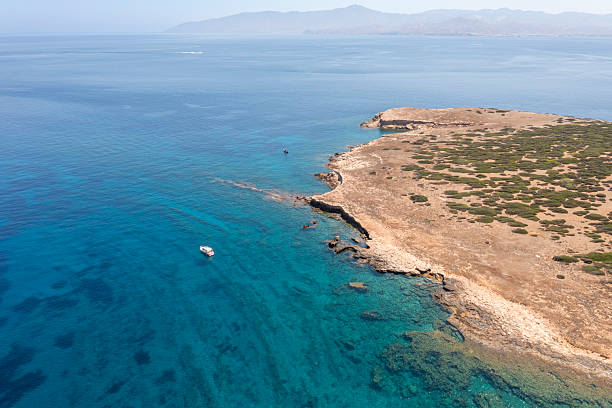 Scenic aerial photo of the coastline near Paros, Greece, showing transparent blue waters, rugged terrain, and the horizon fading into mountainous landscapes.