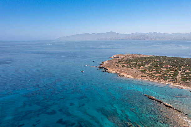Aerial view of a rocky peninsula near Paros, Greece, surrounded by turquoise waters, with distant mountains under a clear summer sky.