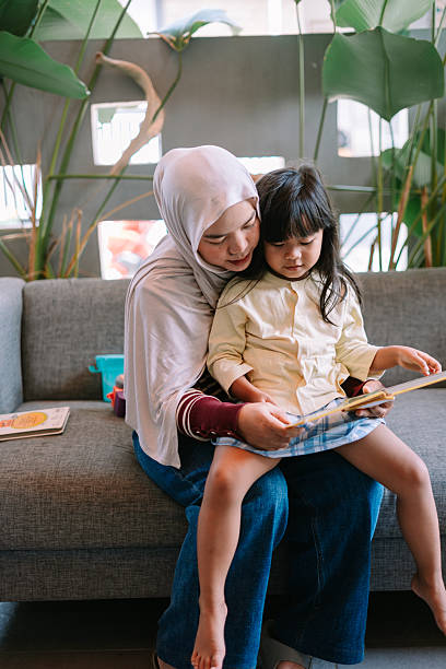istock Caring Mother Reads Storybook with Daughter on Sofa 2247309343