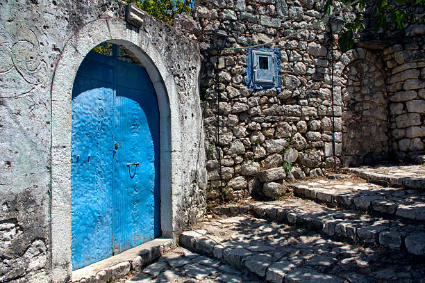 Albania - Himara,  july/12/2025: alleys of the ancient ruined castle of the town of Himare, on the southern coast of Albania: stone walls, abandoned houses, doors and pergolas under the summer sun and a magnificent view of the Ionian Sea