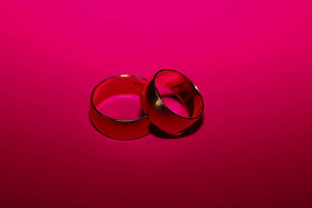 istock Two classic gold wedding rings rest on a rich, vibrant pink (fuchsia) background, creating a contrasting and passionate composition. Bright lighting emphasizes the glossy texture of the metal and symbolizes eternal love, promise, and union. 2247315884