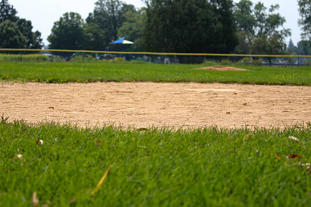 A ground-level view of a baseball field with grass in the foreground and the dirt infield with trees in the distance. sports background with copy space.