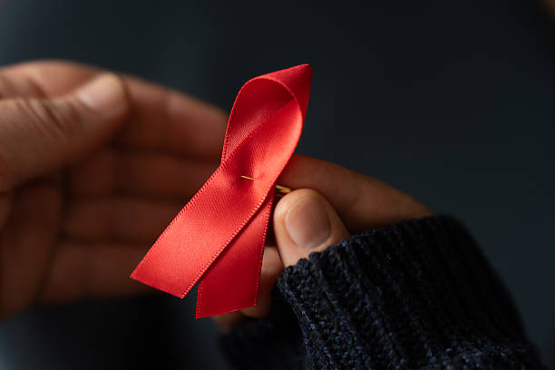 istock An elderly woman's hands hold a red ribbon against AIDS. 2247316469
