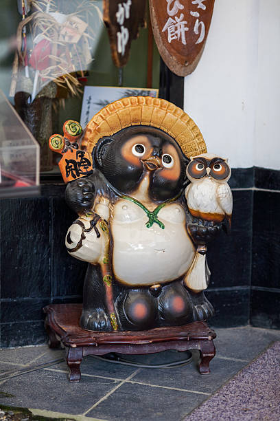 istock Traditional Japanese Ceramic Tanuki Statue Wearing a Straw Hat, Holding a Sake Bottle and an Owl, Symbolizing Good Fortune. 2247318991