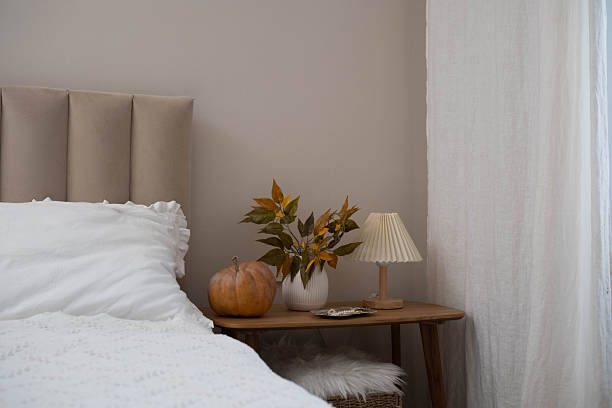 istock Cozy fall decor in a light and bright bedroom, bed, white bed sheets, autumn branches in white vase, lamp, pumpkin on wooden bench. 2247319730