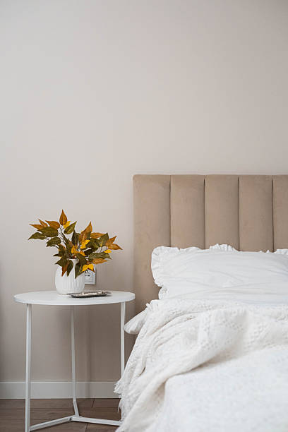 istock Cozy fall decor in a light and bright bedroom, bed, white bed sheets, autumn branches in white vase on white round table. 2247320598