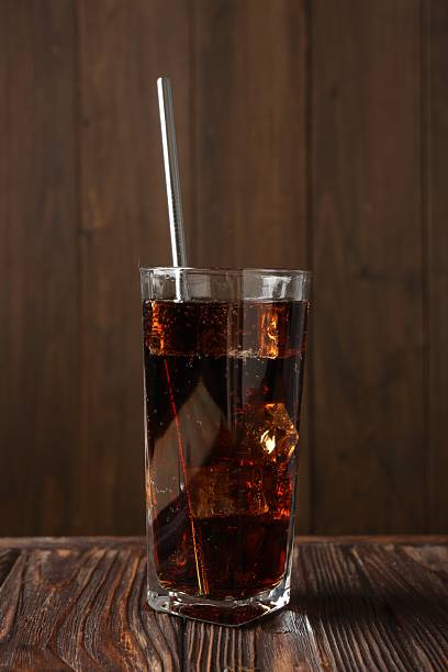 istock Cold cola with ice cubes and drinking straw in glass on wooden table 2247322038