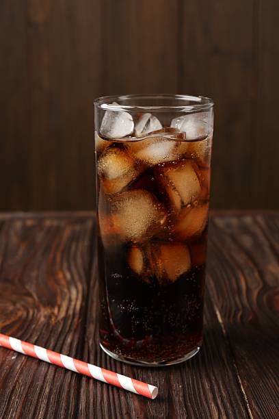 istock Cold cola with ice cubes in glass and drinking straw on wooden table 2247322206
