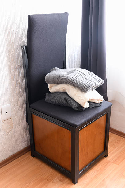 istock Folded Sweaters on Black Storage Bench by Window, ironing board chair 2247323591