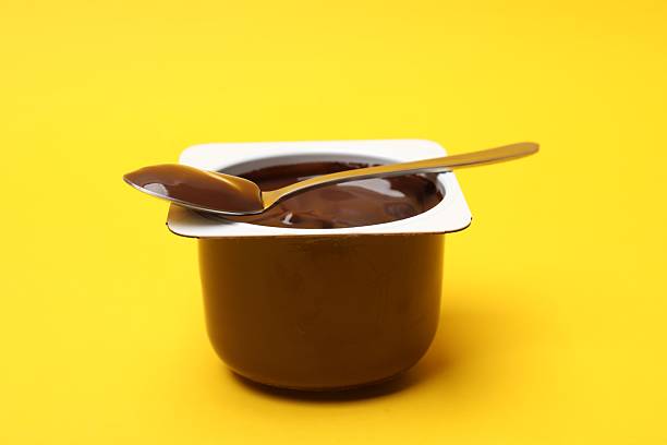 istock Delicious chocolate yogurt in plastic cup with spoon on yellow background, closeup 2247324350