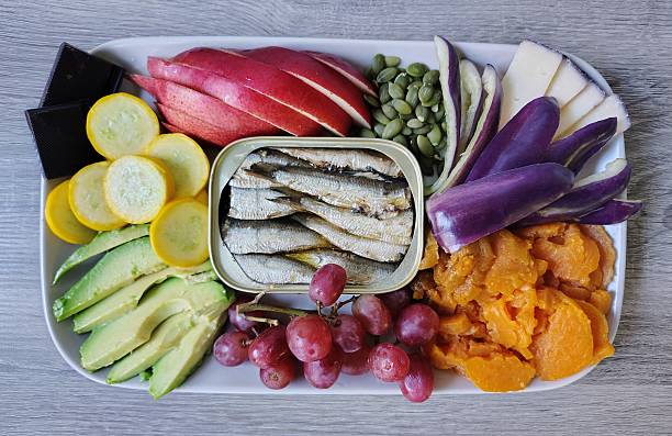 Delicious fresh food, including purple bell pepper, yam, red grapes, avocado, squash, dark chocolate, pear, pumpkin seeds, BellaVitano Merlot cheese, sardines
