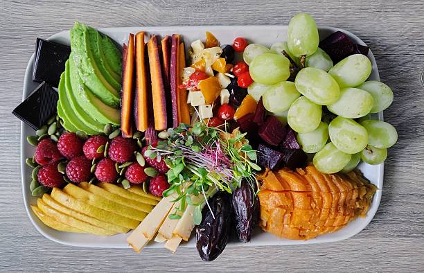 Delicious fresh food, including green grapes, antipasto salad, purple carrots, avocado, dark chocolate, pumpkin seeds, raspberries, microgreens over hummus, BellaVitano cheese, dates, yam, beets, pear