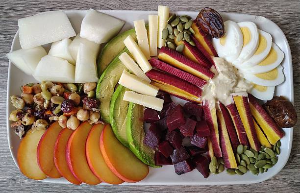 Delicious fresh food, including white melon, garbanzo bean salad, peach, avocado, sharp white cheddar, orange and purple carrots, dates, pumpkin seeds, beets, hummus, egg