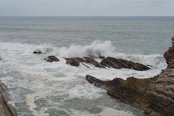 A scenic view of a rugged coastline with steep cliffs and waves crashing against the rocks. The ocean appears deep blue and turquoise under a partly cloudy sky, capturing the beauty and power of nature.