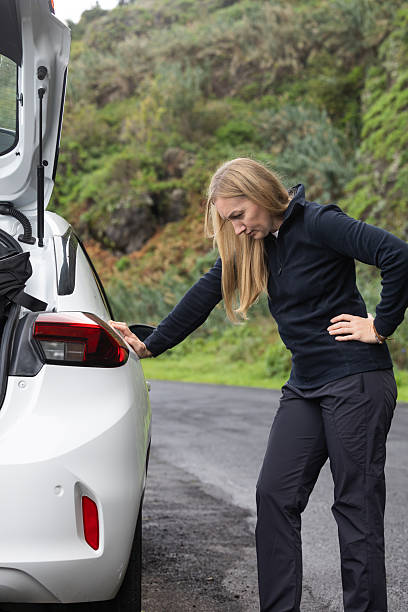 istock Young woman examining her car on the roadside with a concerned expression and natural scenery 2247332695
