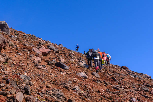 Yuzhno-Kurilsk, Russia September 4, 2025: A group of hikers ascends a steep, rocky slope on a sunny day in Russia. The clear sky offers a stunning backdrop to this adventurous journey through nature.