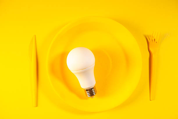 istock Light bulb on yellow plate with fork and knife on yellow background, top view 2247336397