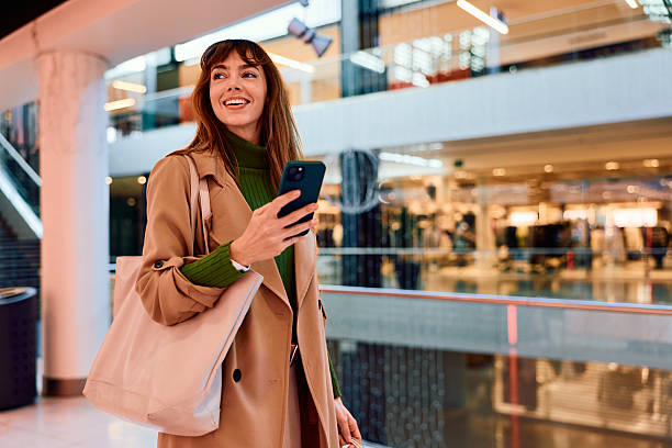 istock Woman smiling holding smartphone walking through shopping mall 2247336421